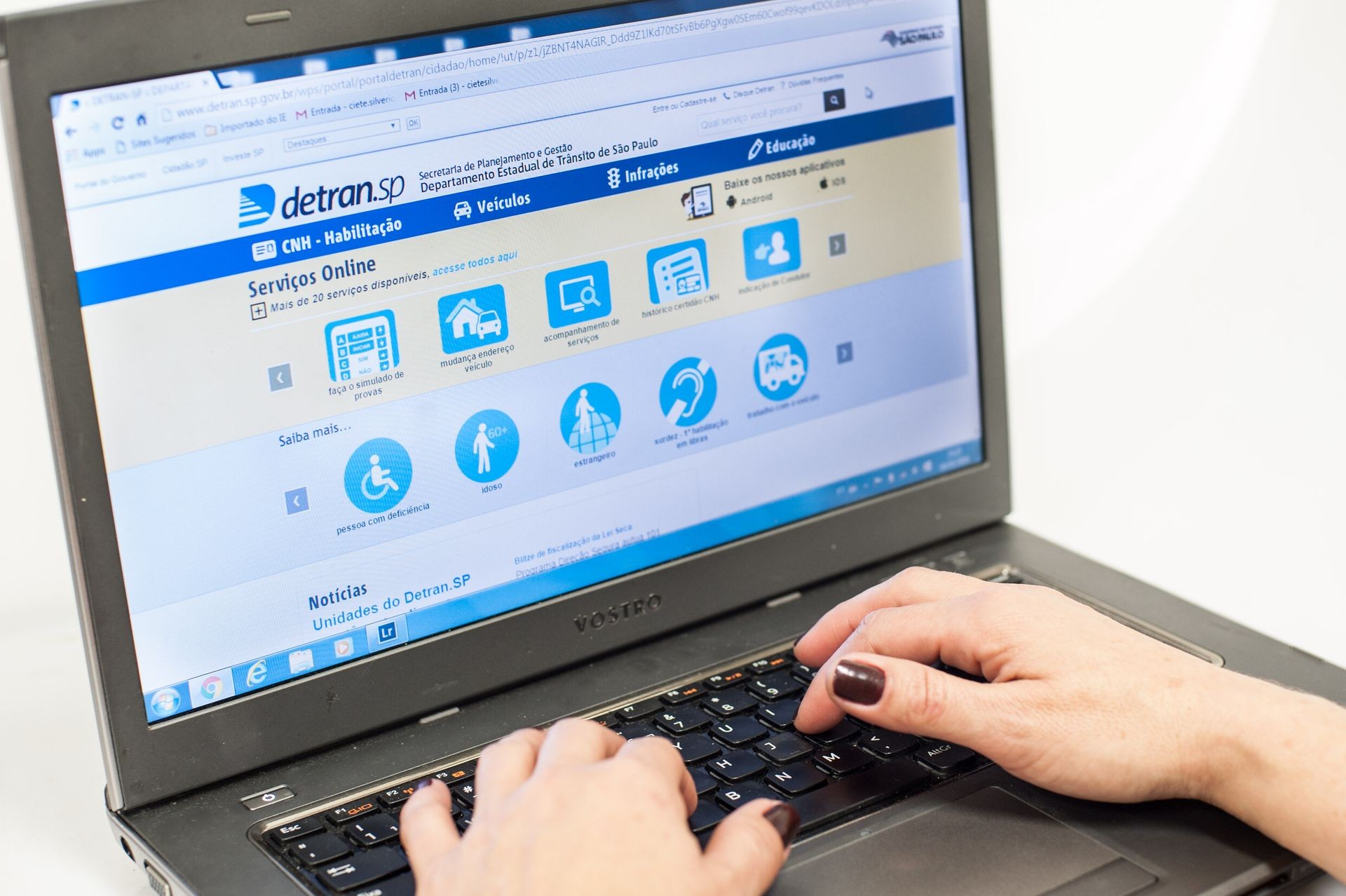 Hands typing on a laptop showing the Detran.SP website with online services menu visible.